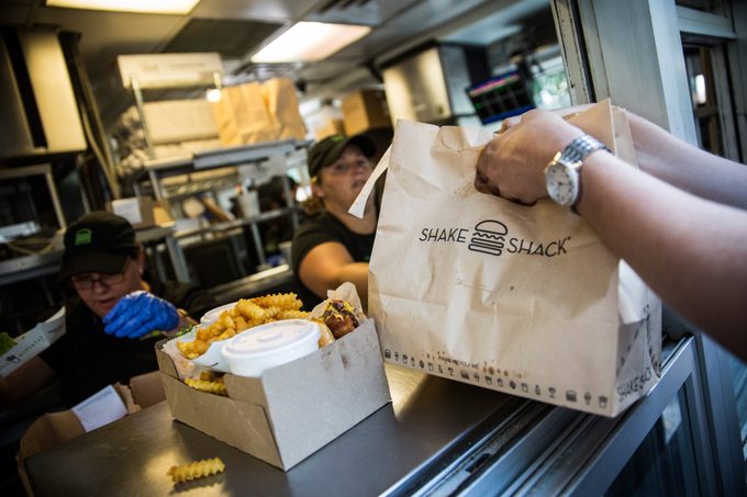 Hands grabbing a Shake Shack takeout bag next to a box of Shake Shack sandwiches and fries