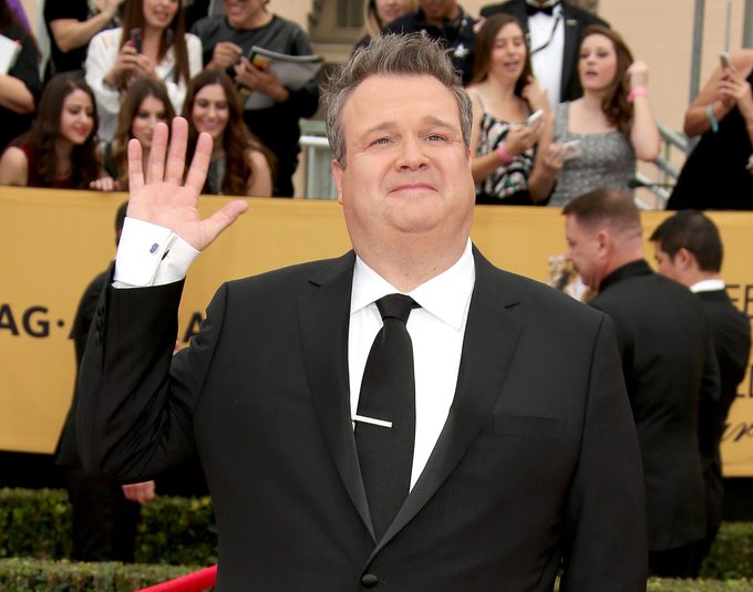 Eric Stonestreet waves on the Screen Actors Guild Awards red carpet wearing a black suit and tie