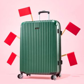 Large green suitcase with red flags around it against a pink background
