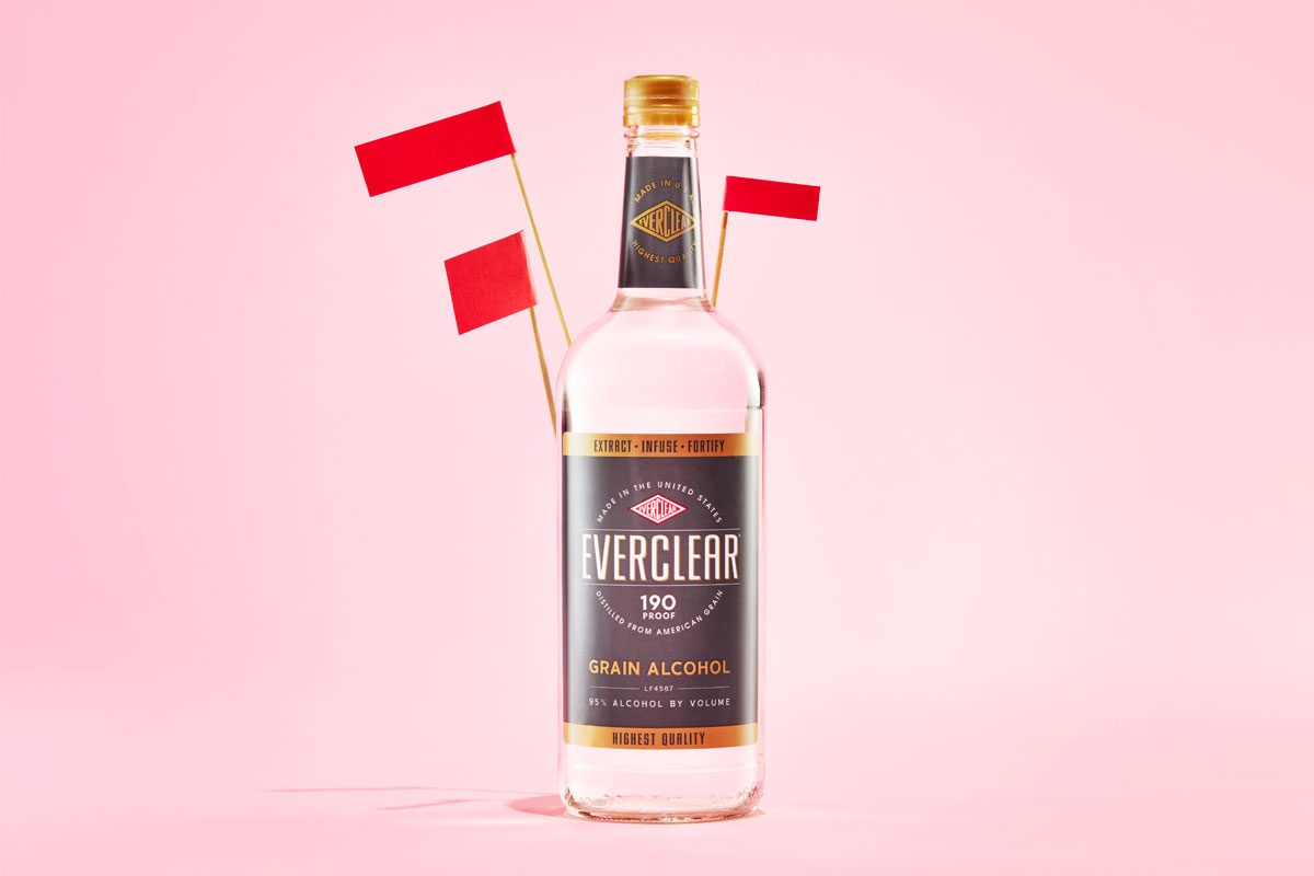 High proof alcohol bottle with red flags against a pink background