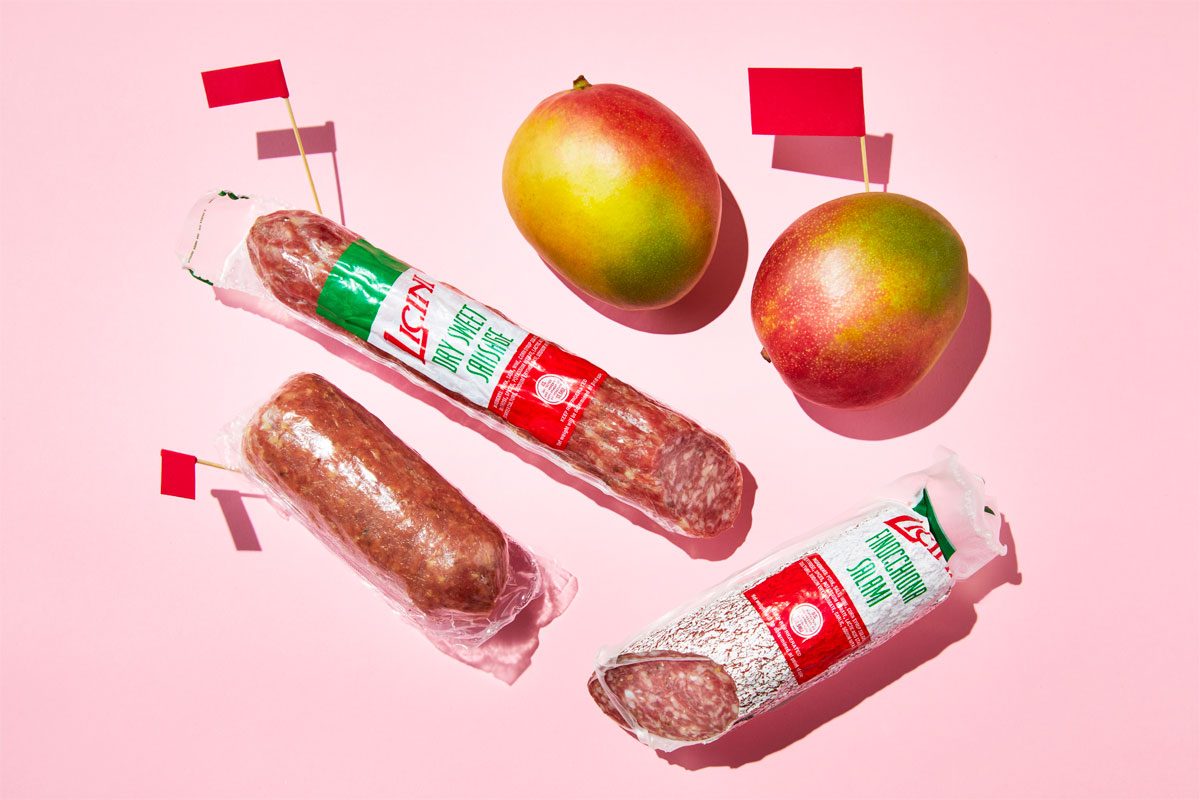 european meat and tropical mangoes with red flags against a pink background