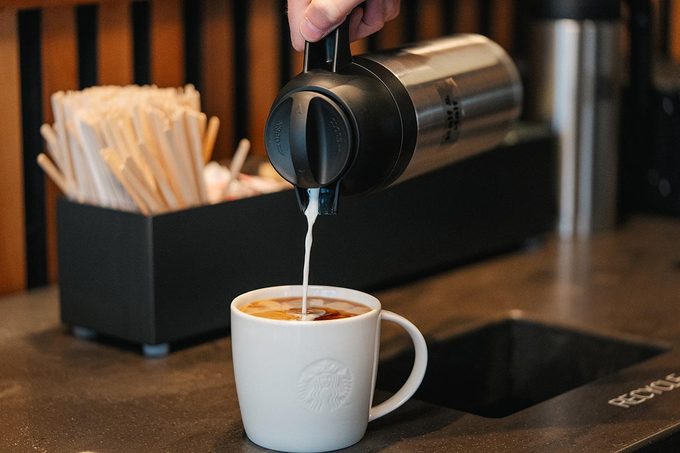 Milk is poured into a ceramic Starbucks mug at a condiment bar