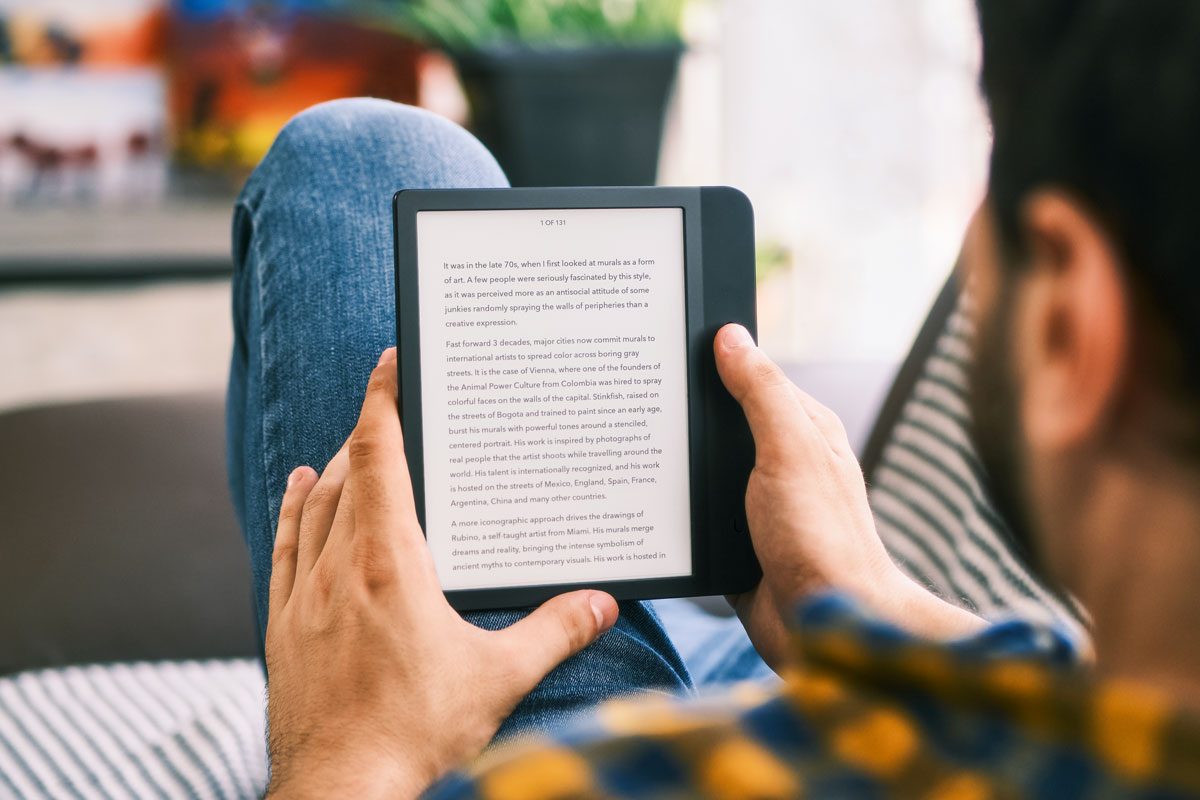 Young Man Holding E Reader And Reading Ebook