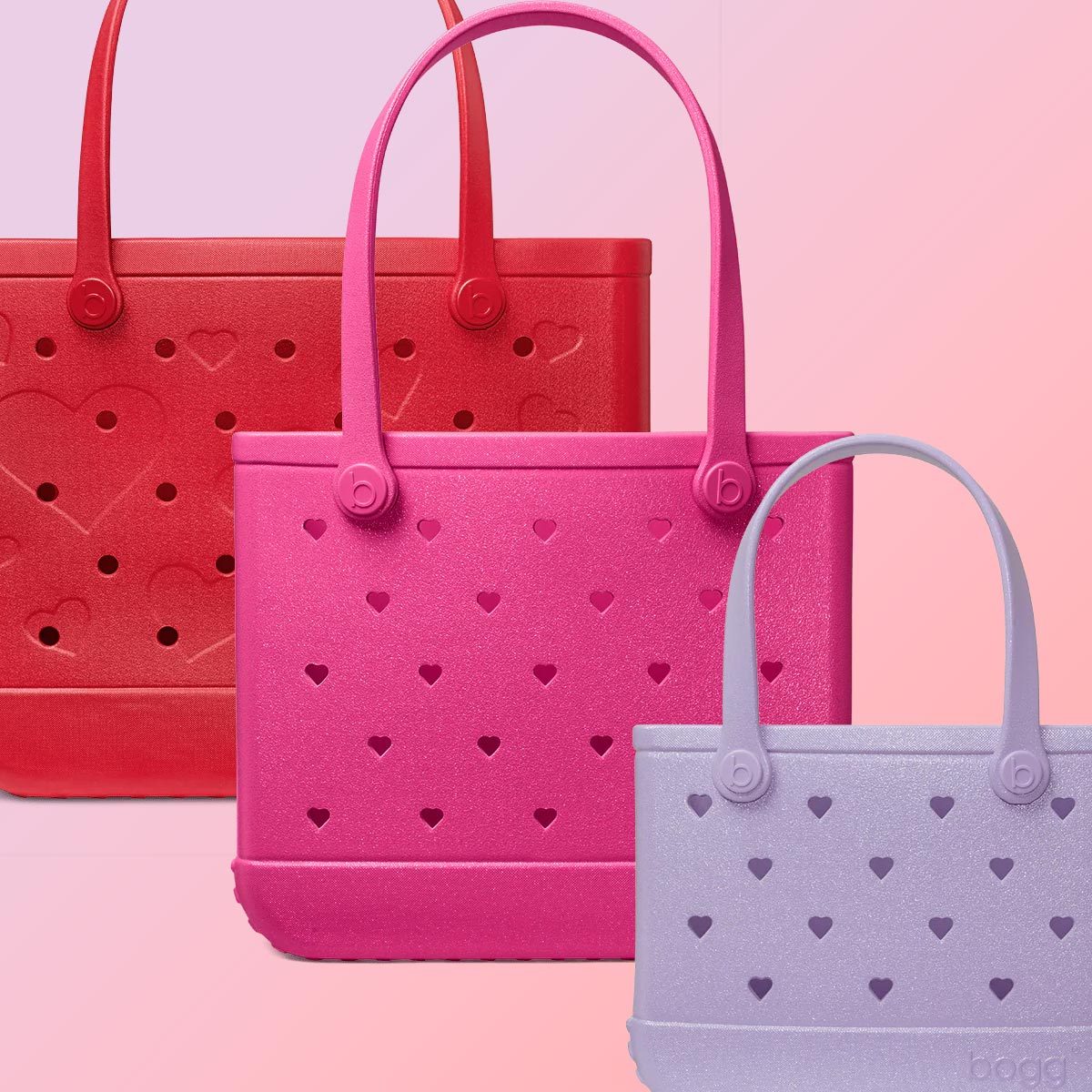 Three Bogg bags of different sizes in red, pink, and lilac, with heart-shaped holes in the sides, on a pink and purple background
