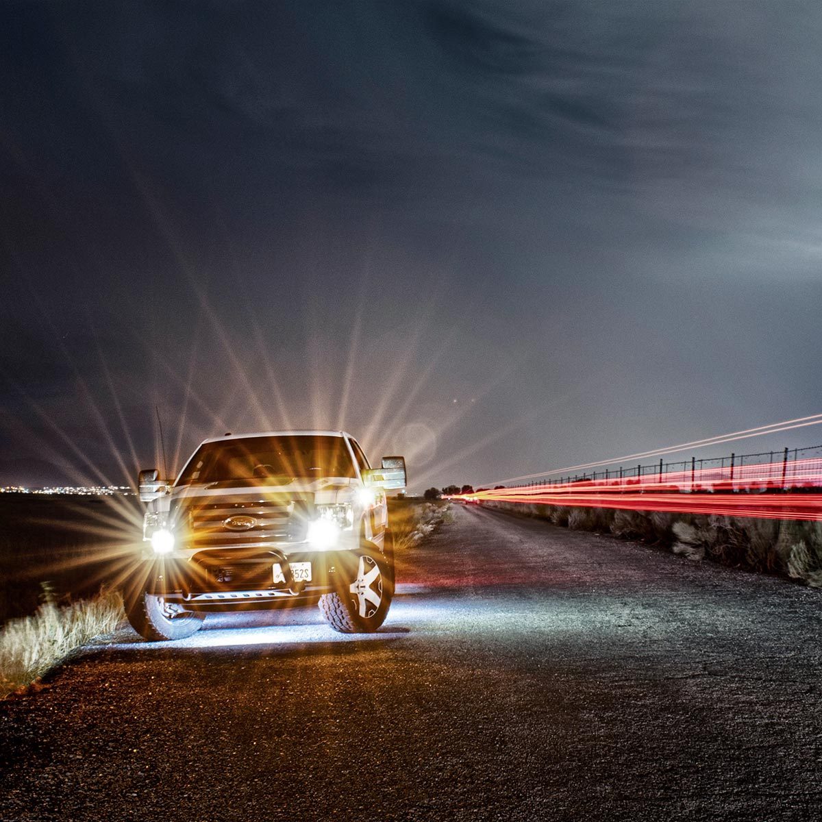 Head-on view of a Ford F150 with bright headlights parked on the street during storm shot in long exposure