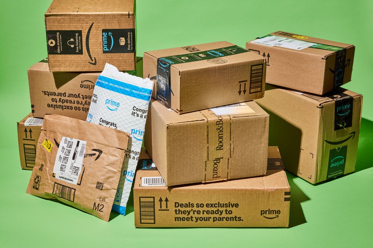 3/4th shot; a pile of cardboard boxes stacked on top of each other; The boxes are of various sizes and shapes, and they all have the Amazon Prime logo on them; Some of the boxes are open and contain items, while others are closed; The background is a solid green color;