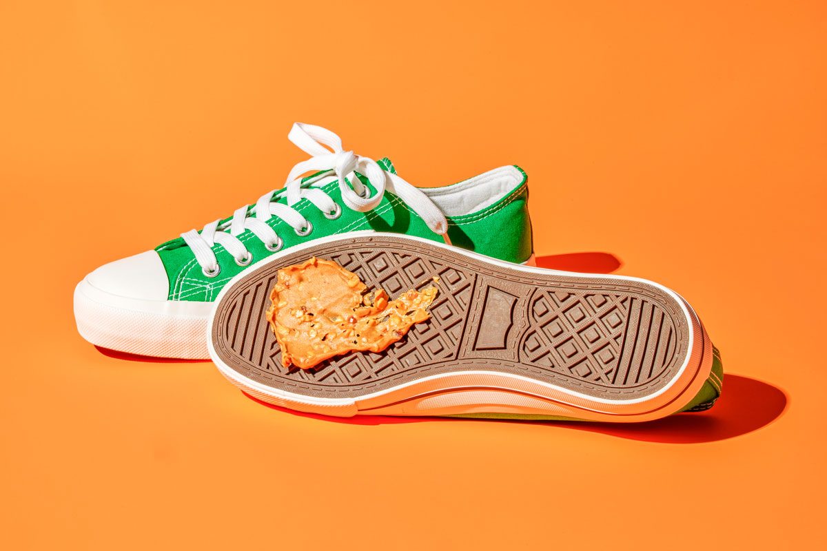 Table view shot of a smudge of crunchy peanut butter on the bottom of a shoe; with the sole facing the camera; orange background;