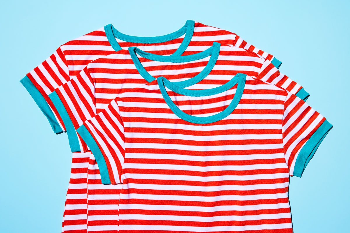 overhead shot; Three identical striped t-shirts are stacked on top of each other against a light blue background; The t-shirts have red and white stripes and teal-colored cuffs and collar;