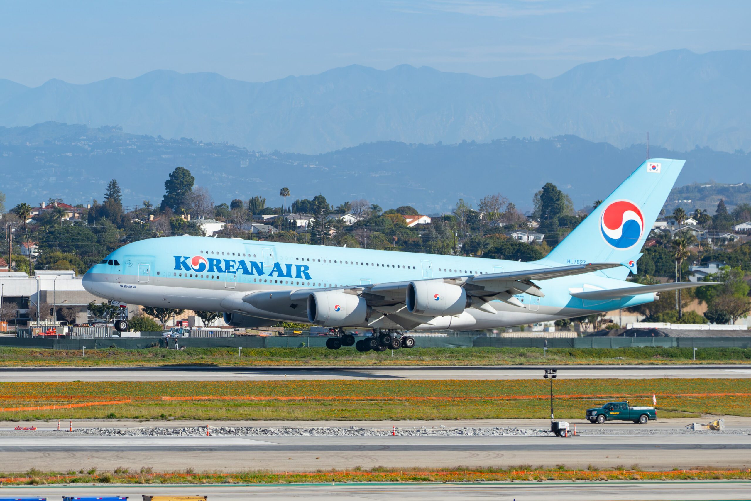 Light blue KoreanAir plane takes off from runway with mountains in background