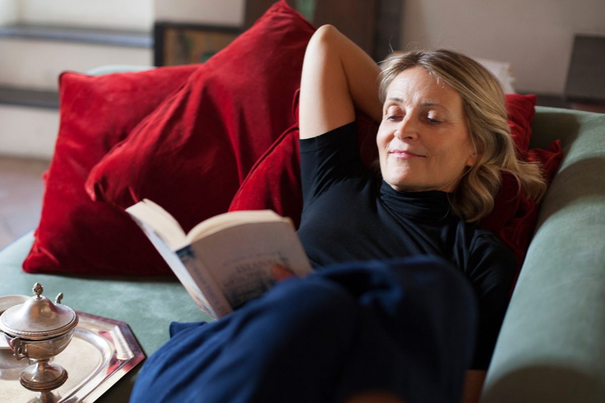 woman grinning while reading a book on sofa