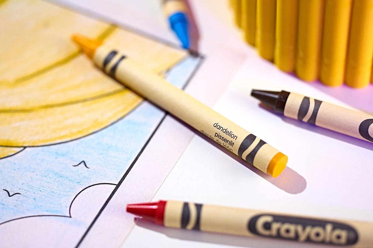 Close-up of Dandelion crayon on a coloring sheet with black, blue, and red crayons nearby