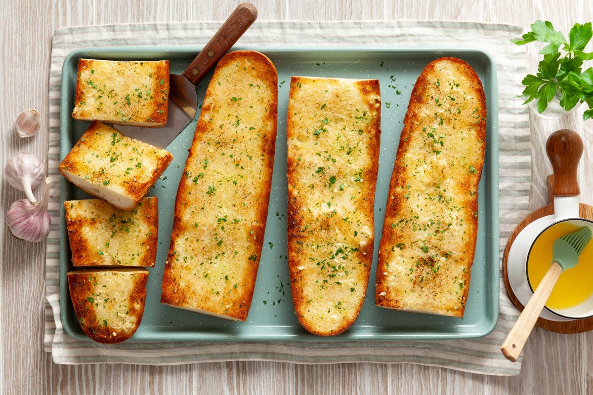 Garlic Bread on a baking sheet with butter and cloves of garlic nearby